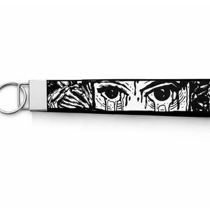 May include: Black and white wristlet keychain with a metal ring. The fabric features a graphic design of a crying eye, a hand, and a skull. The keychain is a wrist strap style.