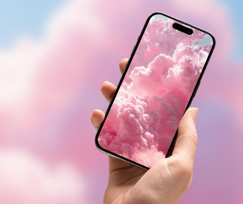 May include: A black smartphone displays a pink cloud wallpaper. The phone is held in a hand against a soft, blurred background of pink and blue hues. The screen shows fluffy, pink clouds.