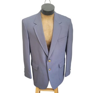 May include: A light blue blazer with two front pockets, gold buttons, and a notched lapel. The blazer is displayed on a mannequin and has a classic, tailored design. The sleeves have buttons at the cuffs.
