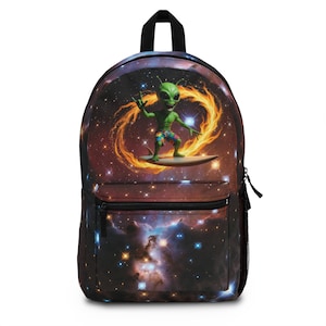 May include: A black backpack featuring a space-themed print of a green alien surfing on a surfboard. The alien wears colorful patterned shorts and makes a hand gesture. The background displays a nebula with bright stars and a swirling orange ring.