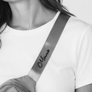 May include: A close-up of a person wearing a white t-shirt with a gray fanny pack. The fanny pack strap has the word "Mommy" in cursive script. The strap is across the person's shoulder.