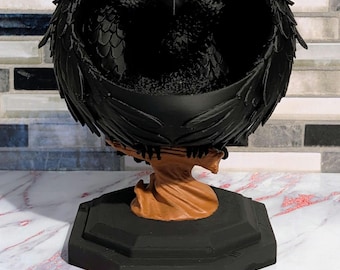May include: A black raven figurine with spread wings forming a bowl shape, perched on a brown tree branch base. The entire structure is supported by a solid black octagonal pedestal, creating a functional container with a detailed bird design.