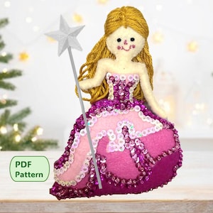May include: A handmade felt princess doll with a blonde yarn hair, a pink and purple sequined dress, and a silver star wand. The doll is a Christmas ornament, with a PDF pattern available.