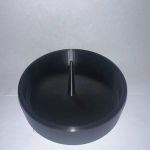 May include: A black candle holder with a circular base and a central spike. The holder is made of a solid, matte material and is designed to hold a single candle. The design is simple and modern.