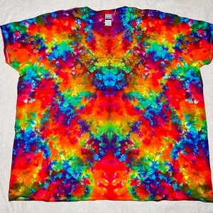 K&ouml;nnte beinhalten: Ein Batik-T-Shirt mit einem farbenfrohen, wirbelnden Muster in Blaut&ouml;nen, Gr&uuml;n, Orange, Rot und Lila.