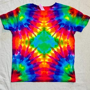 May include: A vibrant tie-dye t-shirt in a kaleidoscope of colors, including red, orange, yellow, green, and blue. The short-sleeved shirt features a symmetrical pattern radiating from the center. The shirt is made of a soft material.
