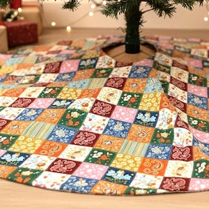 May include: A colorful, patchwork Christmas tree skirt. The skirt features a variety of patterned squares in shades of orange, green, blue, pink, and brown. The skirt has a circular shape with a hole in the center for the tree trunk.