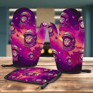 Pode incluir: Um conjunto de acessórios de cozinha com um design de gato espacial. O conjunto inclui duas luvas de forno e um descanso de panela. O design apresenta um gato com um capacete de astronauta em um fundo espacial roxo e rosa.