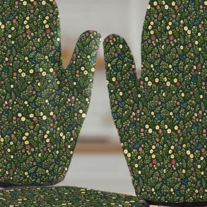 May include: A set of three kitchen items: two oven gloves and a pot holder. The items are dark green with a floral pattern of small yellow, pink, and blue flowers. The gloves have a standard five-finger design.