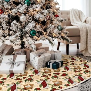 May include: A decorated Christmas tree with ornaments and wrapped gifts beneath it. The tree is covered in faux snow and has various colored ornaments. A cream-colored tree skirt with a religious design is at the base of the tree.