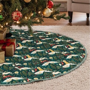 May include: A round Christmas tree skirt with a forest and deer pattern in shades of green, white, and red. The skirt is placed under a decorated Christmas tree with ornaments and lights. The edge of the skirt is trimmed with a light green border.