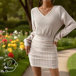 May include: A beige ribbed knit dress with a V-neck and long sleeves. The dress features a ruched skirt and a fitted waist. The image is set against a backdrop of a garden with colorful flowers and green grass. The logo "DRESSINGIUM" is in the bottom left corner.