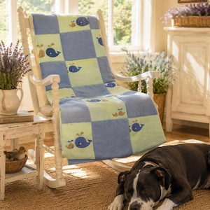 May include: A patchwork quilt featuring a repeating checkerboard pattern of light green and blue squares. The quilt is decorated with small, embroidered illustrations of blue and tan whales, each depicted with a water spout above its head.