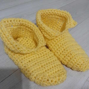 Pu&ograve; includere: Un paio di pantofole all'uncinetto gialle fatte a mano. Le pantofole hanno uno stile stivaletto con un risvolto. La maglia all'uncinetto crea una superficie strutturata. Le pantofole sono progettate per l'uso in casa.