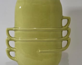 May include: A stacked ceramic vase in a pale green color. The vase is composed of three cup-shaped sections with handles, and a top section. The design is modern and minimalist.