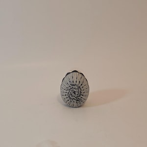 May include: A ceramic egg-shaped decorative object. The object is white with a black radial pattern. The pattern radiates from the center of the egg, with thin black lines. The top edge has a scalloped design.