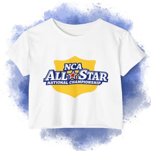 May include: White crop top with a crew neck and short sleeves. The shirt features a yellow shield design with the text "NCA ALL STAR NATIONAL CHAMPIONSHIP" in blue and white.