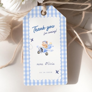 Puede incluir: Una etiqueta de regalo a cuadros azules y blancos con el texto "Thank you for coming!" en escritura azul. Presenta una ilustración de un oso de peluche en un avión azul. La etiqueta también incluye el nombre "Olivia" y la fecha "10.14.20XX".