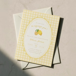 Könnte beinhalten: Eine Babyparty-Einladung mit gelbem Vichy-Karo-Hintergrund. Die Einladung zeigt ein ovales Design mit Zitronen und dem Text "We can't wait to squeeze you!". Sie liegt auf einem weißen Umschlag.