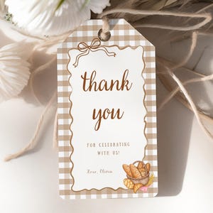 May include: A rectangular gift tag with a brown and white gingham border and a decorative bow at the top. The tag reads "thank you" in a script font, with additional text below. A watercolour illustration of bread and a basket is at the bottom.