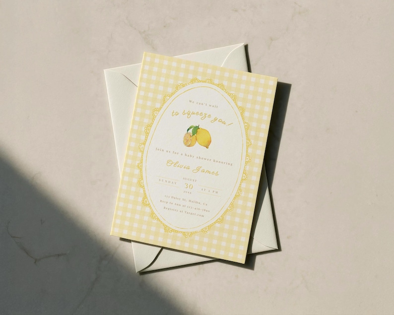 May include: A baby shower invitation with a yellow gingham pattern background. The invitation features an oval design with lemons and the text "We can't wait to squeeze you!" The invitation is on top of a white envelope.