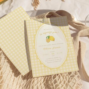May include: Baby shower invitations with a yellow gingham pattern. The invitation features text in a decorative oval frame with lemon illustrations. The text reads "We can't wait to squeeze you!" and includes the name Olivia James.