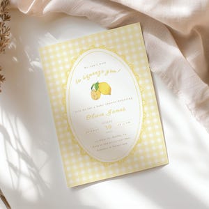 May include: A baby shower invitation with a yellow gingham background. The invitation features an oval design with a lemon illustration and the text "We can't wait to squeeze you!" The invitation is for Olivia James, August 30.