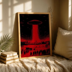 Puede incluir: Impresión artística enmarcada que representa una escena roja y negra de un OVNI que proyecta un rayo rojo sobre una multitud. La obra de arte está en un marco de madera y se exhibe en una cama con una colcha de color neutro.