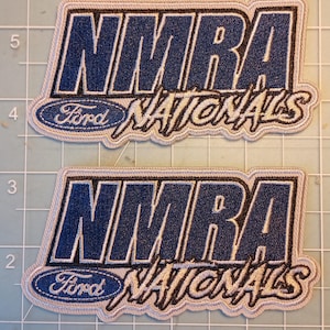May include: Two embroidered patches with the text "NMRA Nationals" in navy blue and white. The Ford logo is featured below the NMRA text. The patches have a light gray border and are on a grid background.