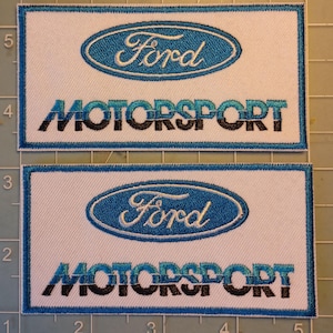 May include: Two embroidered patches with the Ford logo in blue and white. The word "Ford" is in a blue oval, and "MOTORSPORT" is below in blue and black. The patches are rectangular with a white background.