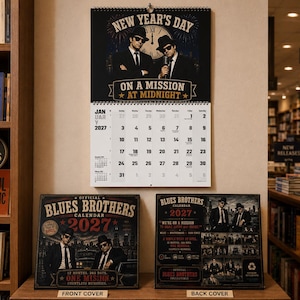 以下が含まれることがあります： ブルース・ブラザーズのグッズの展示。 「New Year's Day」と「On a Mission at Midnight」の文字が入ったカレンダーが、2つのカレンダーカバーの上に吊り下げられています。 表紙には「Blues Brothers Calendar 2027」と書かれています。 裏表紙にもブルース・ブラザーズが描かれています。