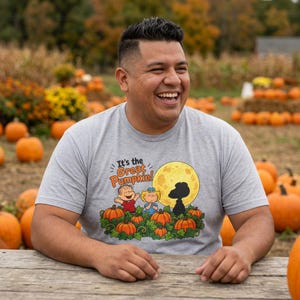 May include: A heather gray short-sleeve t-shirt featuring a graphic of Linus, Lucy, and Snoopy in a pumpkin patch under a full moon. The text reads, It's the Great Pumpkin! The design includes orange pumpkins, green vines, and a yellow moon.