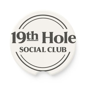 May include: A round, off-white car coaster with a black graphic. The text "19th Hole SOCIAL CLUB" is centered within a black circular design. The coaster has a small notch on one side.