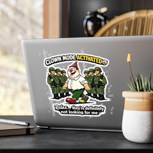 Puede incluir: Una pegatina en un portátil muestra un payaso de dibujos animados caminando frente a soldados. El texto "CLOWN MODE ACTIVATED" y "Relax... they're definitely not looking for me" también están presentes. El payaso lleva un gorro de fiesta.