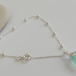 May include: A silver chain bracelet with small silver beads and a light blue sea glass pendant.