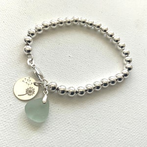May include: A silver beaded bracelet with a silver charm featuring a dandelion design and a light green sea glass charm.