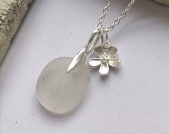 Può includere: Una collana d'argento con un ciondolo in vetro di mare bianco e un ciondolo a forma di fiore d'argento.