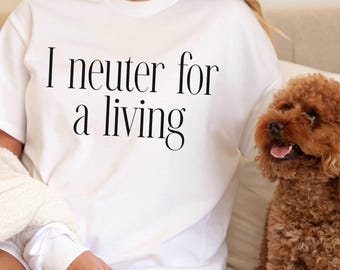May include: White t-shirt with the text "I neuter for a living" in black. A small, brown dog sits next to the person wearing the shirt. The shirt is part of a casual clothing collection.