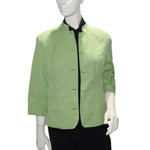 May include: A light green jacket with a mandarin collar and three-quarter sleeves. The jacket has a button-up front and is displayed on a mannequin. The jacket is paired with a black top and black pants.