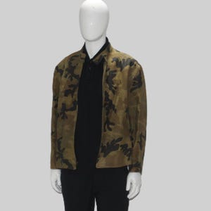 May include: A camouflage-patterned jacket in shades of brown and green, with black accents. The jacket has a zipper closure and is worn over a black collared shirt. The mannequin is wearing black pants.