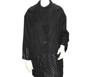 May include: Black wool coat with a classic lapel collar and a single button closure. The coat features a unique design with textured leather-like panels at the hem and cuffs. The coat is displayed on a mannequin.
