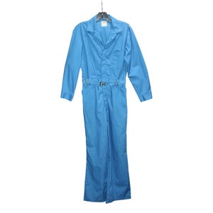 May include: A light blue jumpsuit with long sleeves, a collared neckline, and a front button closure. The jumpsuit features a belt with a silver buckle and a single chest pocket. The garment is hanging on a black hanger.