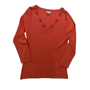 Peut inclure: Un pull-over rouge-orangé à manches longues avec un col en V. L'encolure est ornée d'un motif de perles avec des accents noirs et dorés. Le pull a un design simple et classique, adapté à diverses occasions.
