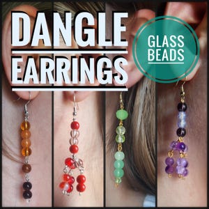 Puede incluir: Pendientes colgantes con cuentas de vidrio de varios colores. Los pendientes incluyen cuentas naranjas, rojas, verdes y moradas. La imagen tiene el texto "DANGLE EARRINGS" y "GLASS BEADS".