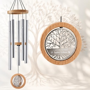May include: A wind chime featuring five silver-toned metal tubes suspended from a circular wooden top. A circular wooden frame hangs at the bottom, enclosing a silver metal tree emblem with the text IN LOVING MEMORY Sophia William 1957-2026.
