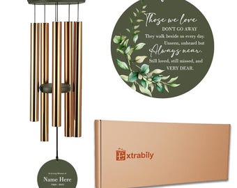 May include: A memorial wind chime with six copper-colored metal tubes, a dark green wooden top, and two circular green plaques. One plaque features the text: Those we love DON'T GO AWAY They walk beside us every day. Unseen, unheard but Always near. Still loved, still missed, and VERY DEAR. The other plaque reads: In Loving Memory of Name Here 1960-2023. A brown cardboard box with the text Extrably is included.