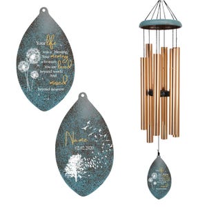 May include: A wind chime with a teal and bronze finish. The wind chime has bronze-colored tubes and a teal top. Two teal leaf-shaped plaques with text and illustrations are also included. One plaque reads "Your life was a blessing."