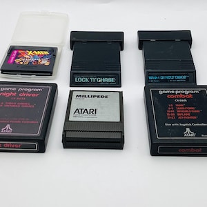 May include: A selection of retro video game cartridges, featuring titles such as "X-Men," "Night Driver," "Millipede," and "Combat." The cartridges are black with vibrant labels and text. Some are in protective cases.