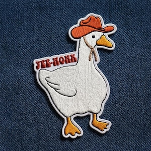 May include: Embroidered patch featuring a white goose wearing an orange cowboy hat. The goose has an orange beak and feet. The text "YEE-HONK" is above the goose's body in red letters. The patch is outlined in white.