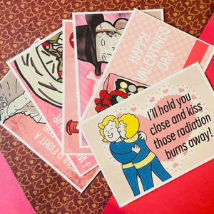 Peut inclure: Plusieurs cartes de Saint-Valentin avec des illustrations et du texte variés. Les cartes présentent des images d'un vampire, d'une pizza et d'un couple qui s'embrasse. Une carte dit "I'll hold you close and kiss those radiation burns away!"